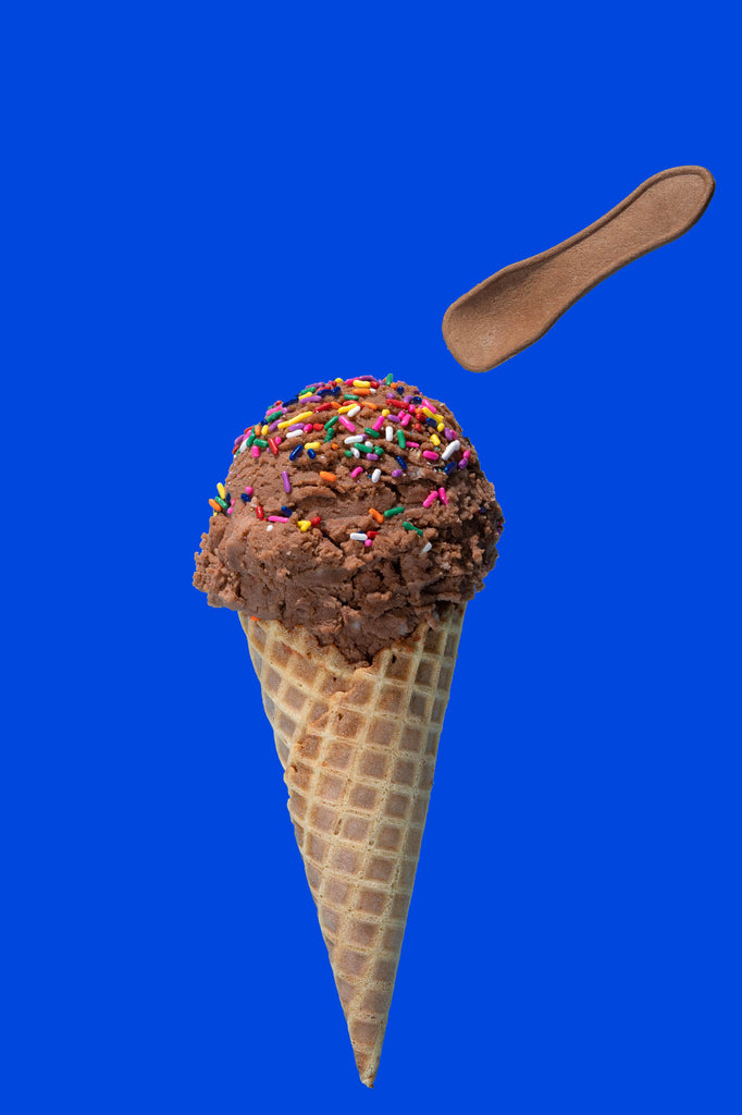 A photo of a small edible spoon above a chocolate ice cream cone. The ice cream is on a dark blue background.